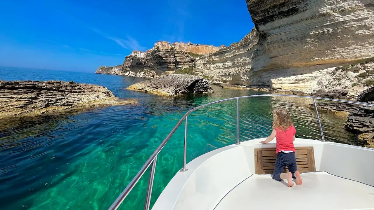 enfant à l'avant du bateau regardant les falaises de Bonifacio lors d'une promenade en mer