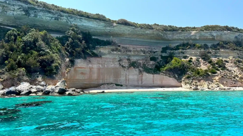 Paroi rocheuse aux teintes rosées dominant la crique de Balistra, couleurs clairs et eaux turquoises à Bonifacio